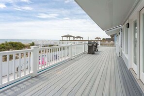 A wooden deck with a white railing, overlooking a beach with umbrellas and gazebos. - Beachfront, Heated POOL, Golf Cart & EV Charging (Ocean Isle Beach)