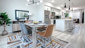 Una cocina moderna con electrodomésticos de acero inoxidable, un comedor con mesa de vidrio y una barra con taburetes.