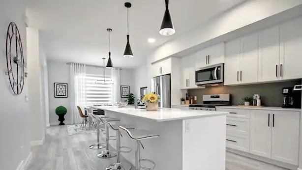Una cocina moderna con gabinetes blancos, electrodomésticos de acero inoxidable y una isla central con taburetes de bar.