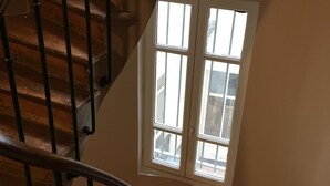 A spiral staircase with wooden steps and black balusters, leading to a landing with a window that offers a view of the outside. - Renovated terrace apartment in Montmartre (Paris)