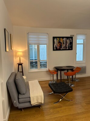 Ein Wohnzimmer mit einer Couch, einem Hocker, einem Tisch, Stühlen und einem Gemälde an der Wand.