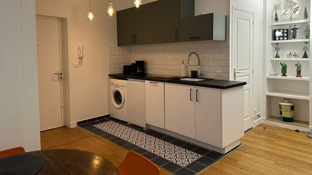 A compact kitchen with white cabinets, a washing machine, a coffee maker, and a sink. - Renovated terrace apartment in Montmartre (Paris)