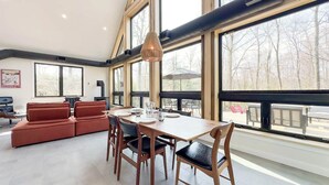 En matplats med ett träbord och stolar, en röd soffa och stora fönster som ger utsikt över omgivningen.