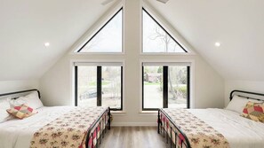 Un dormitorio con dos camas, ventanas amplias y techo inclinado.