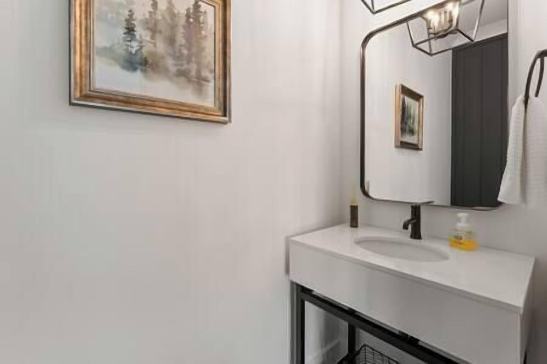 Une salle de bain moderne avec un lavabo blanc, un miroir et un tableau encadré au mur.