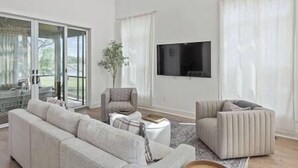 Ein modernes Wohnzimmer mit einer Couch, Sesseln, einem Couchtisch und einem Fernseher.