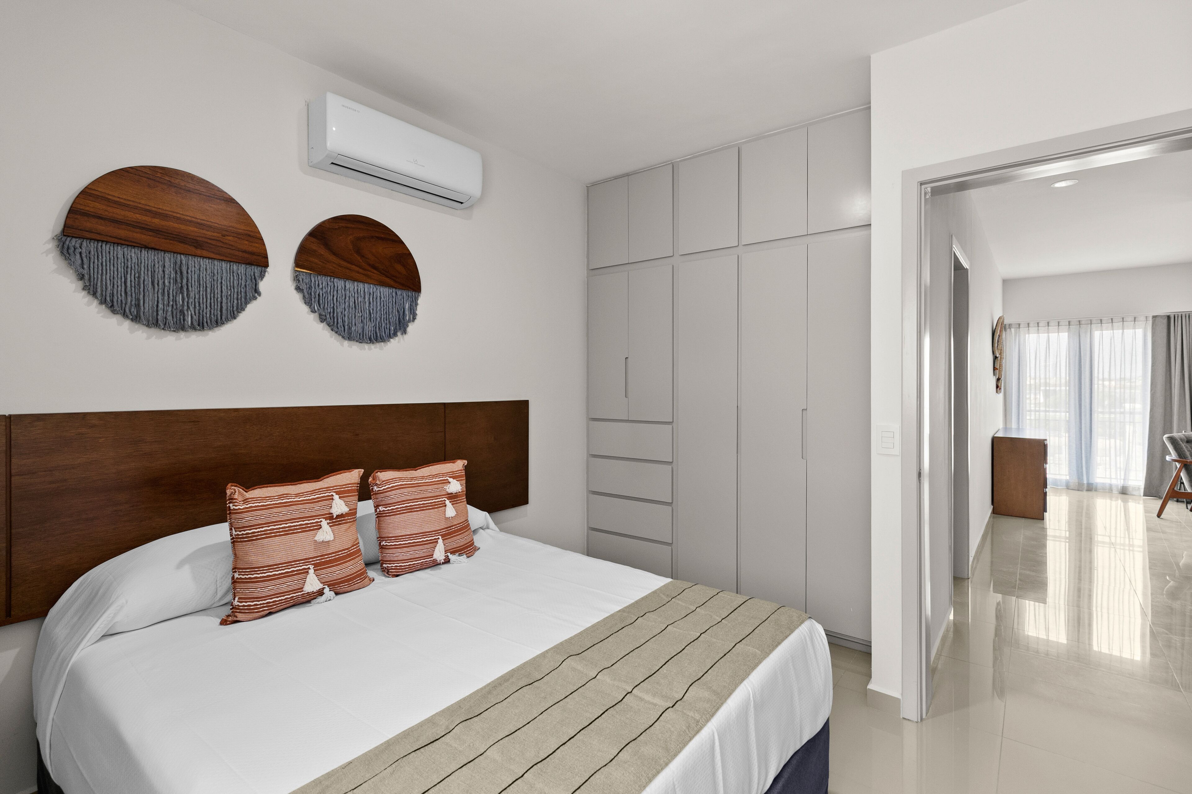 Un dormitorio moderno con una cama grande, un cabecero de madera, un armario y vistas de la habitación contigua.