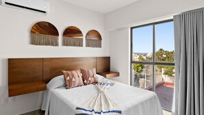 A hotel room with a large bed, a wooden headboard, a view of the city through a large window, and a balcony with a view of the street. - Casa Barros Vacation Condos (Mazatlán)