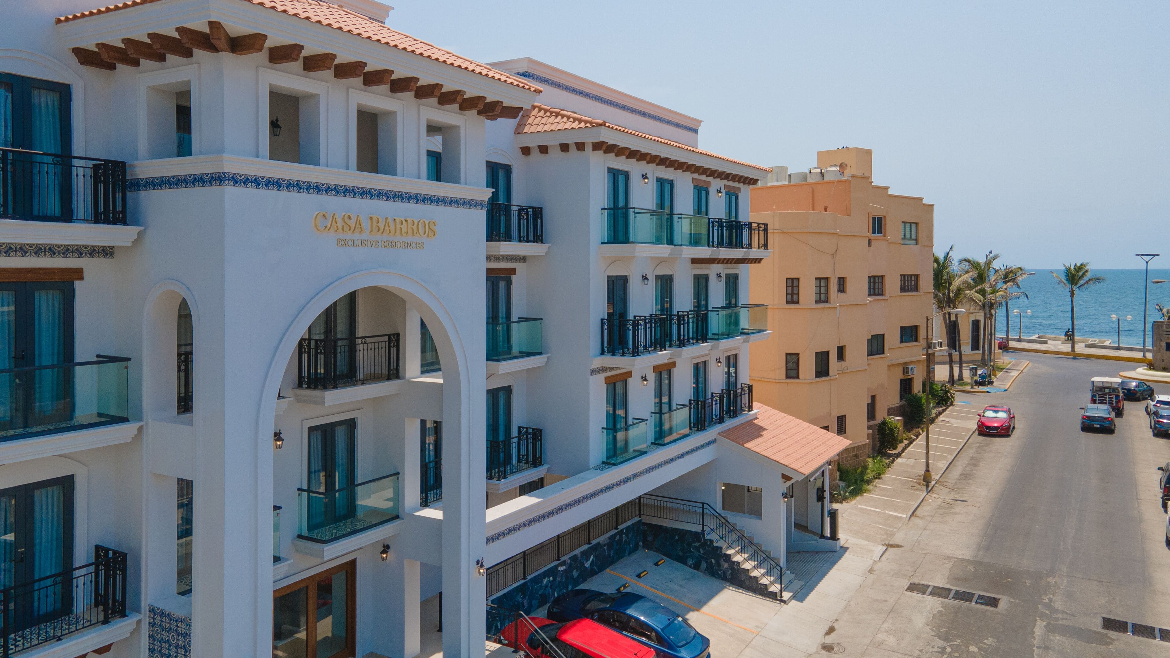 A multi-story hotel with balconies, a parking area, and a view of the sea.