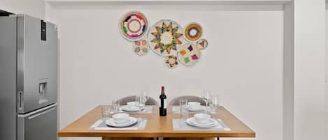 A modern kitchen with a stainless steel refrigerator, a wooden dining table set for four, and decorative wall art.