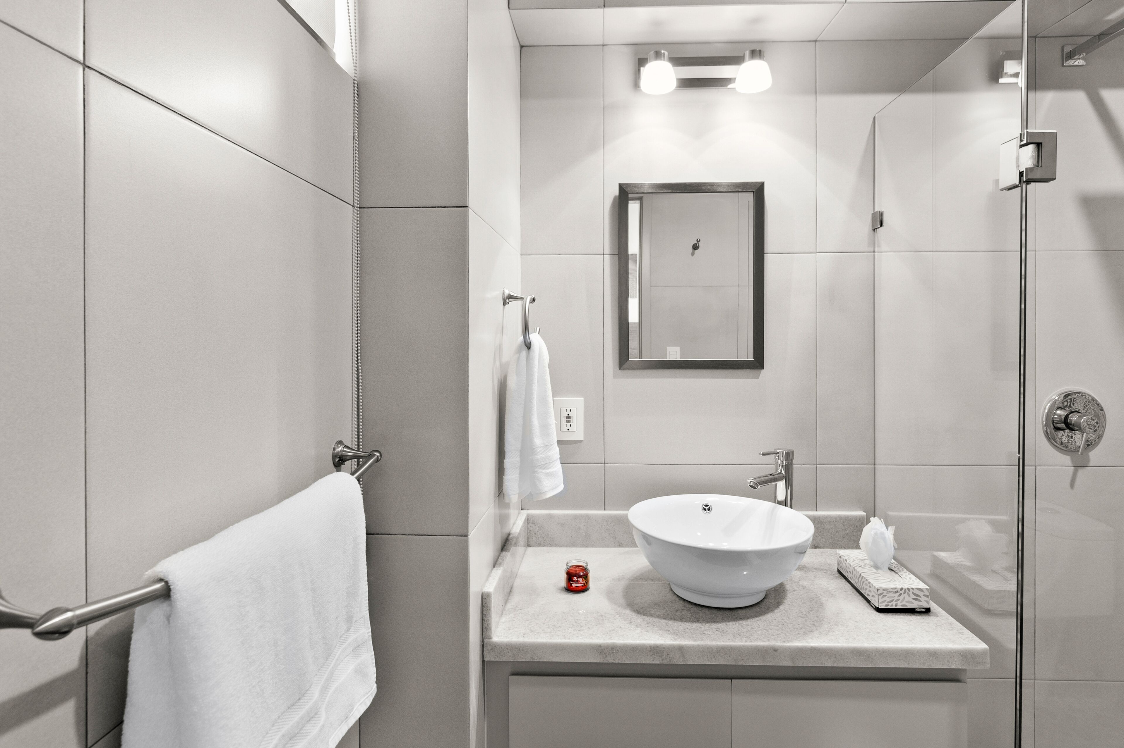 A modern bathroom with a large mirror, a white sink, and a glass shower enclosure.