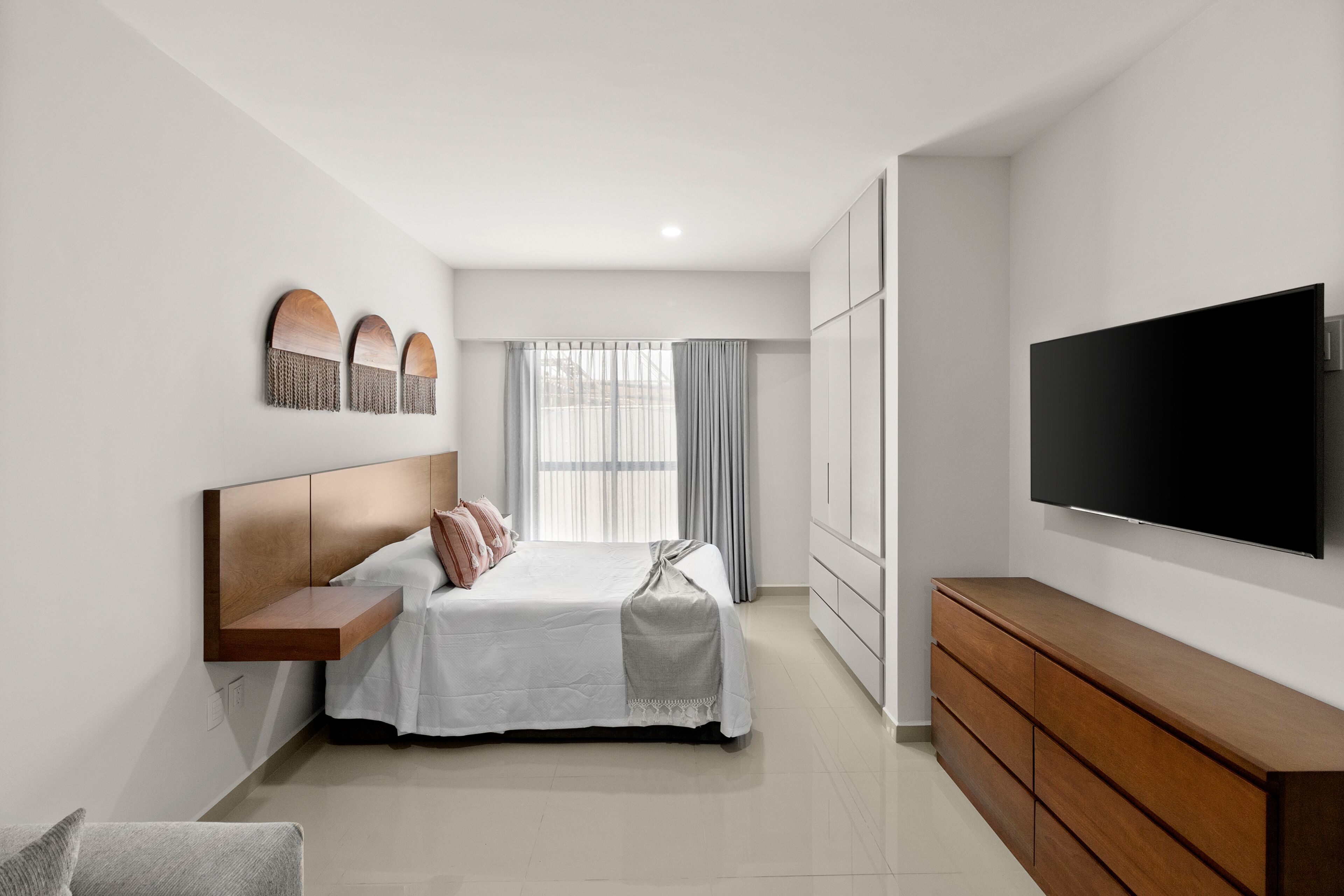 Une chambre à coucher moderne avec un lit, une télévision et une commode en bois.