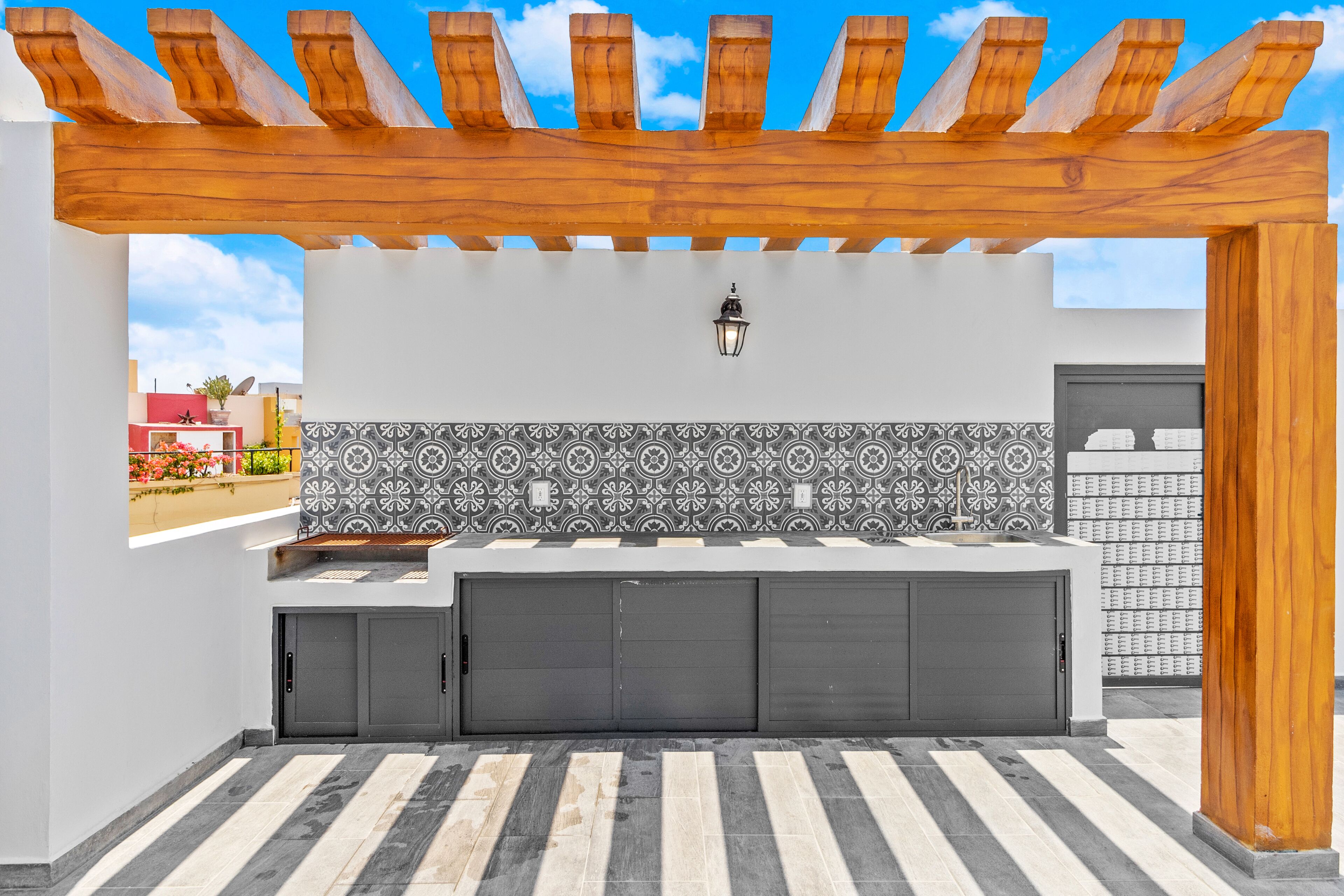 A modern kitchen with a tiled backsplash, a built-in oven, and a pergola overhead.