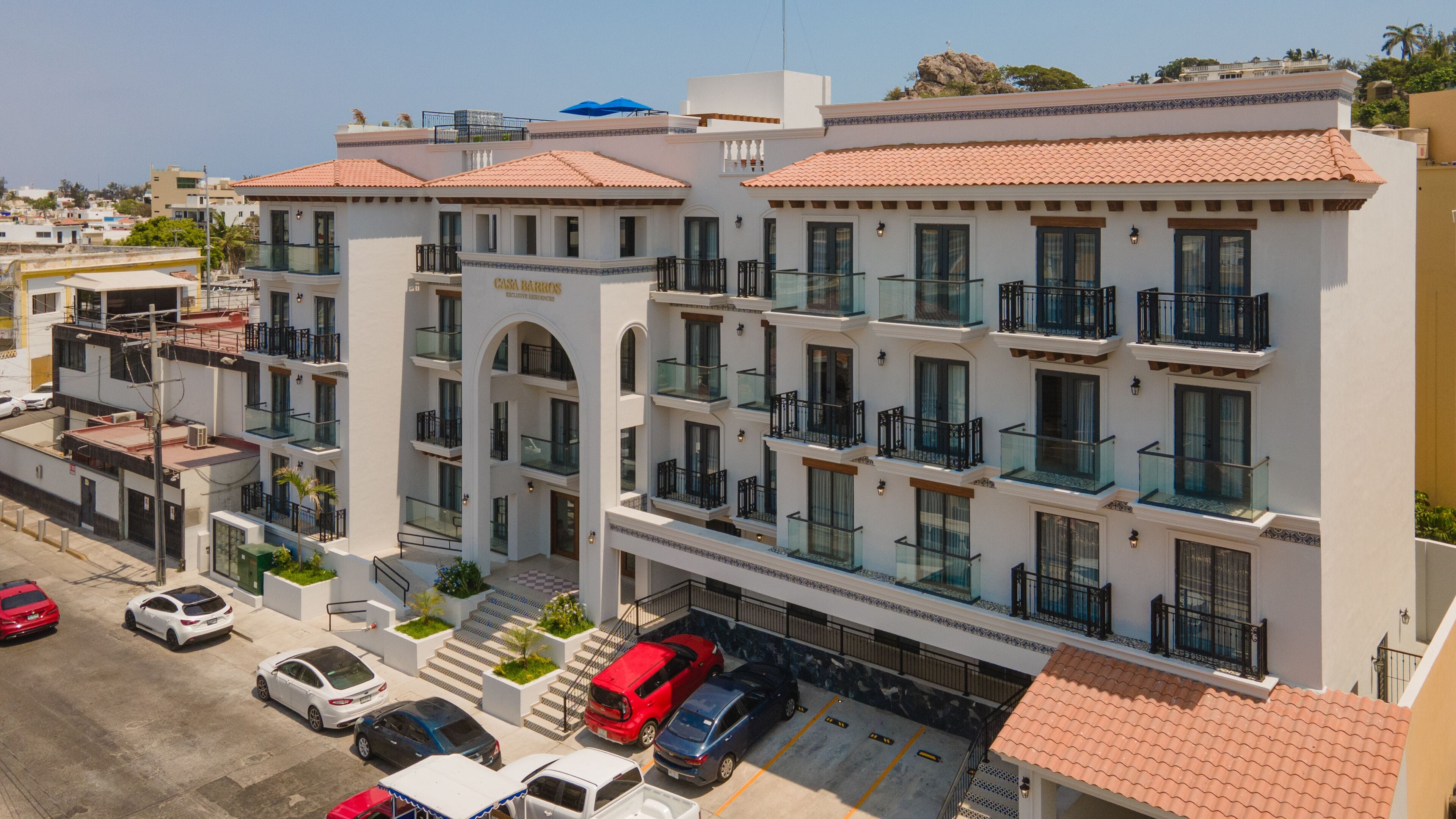 A multi-story hotel with a central courtyard, balconies, and a parking area.