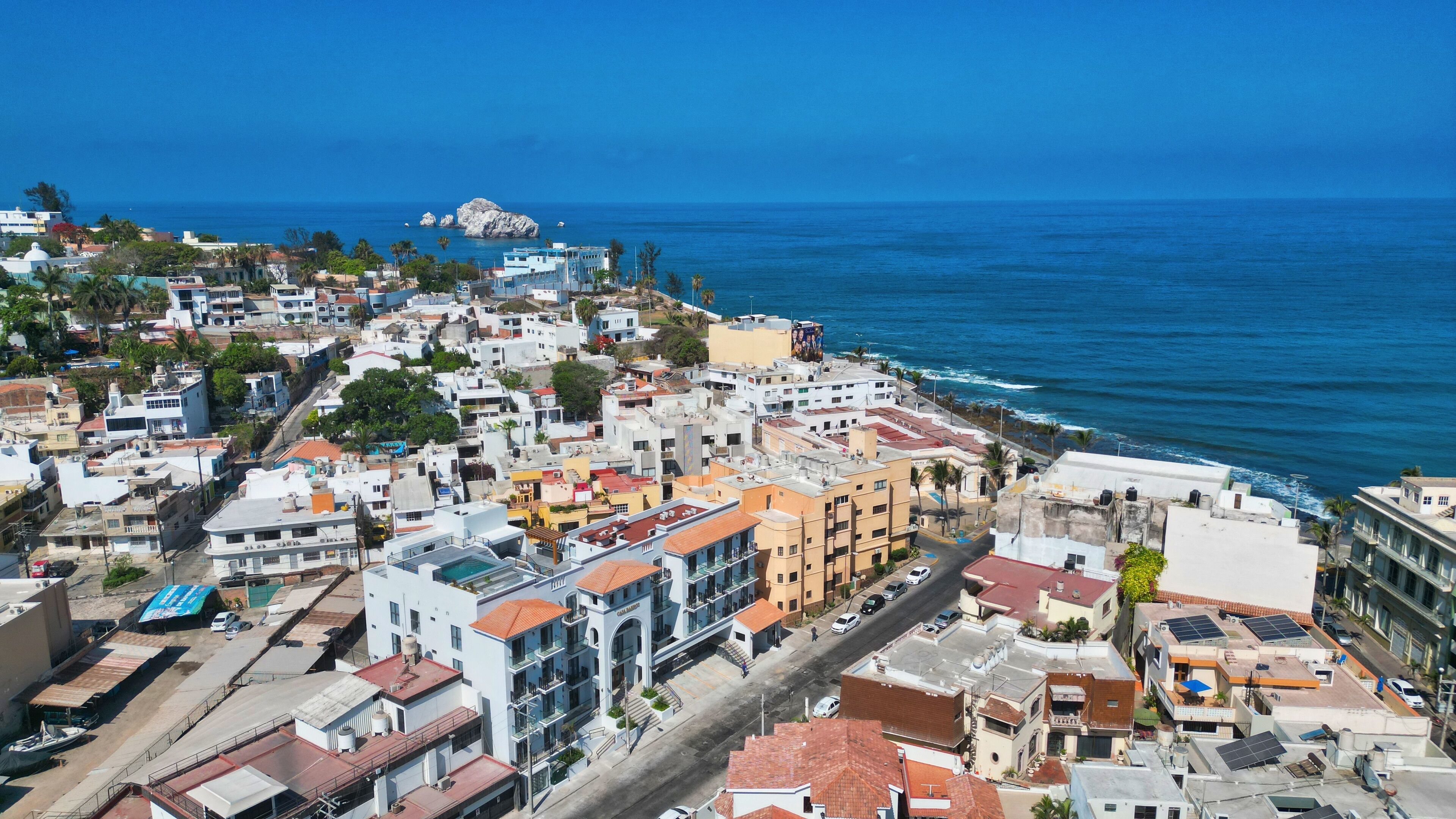 A coastal cityscape with a mix of residential and commercial buildings, a prominent white building with a red roof, and a view of the ocean.