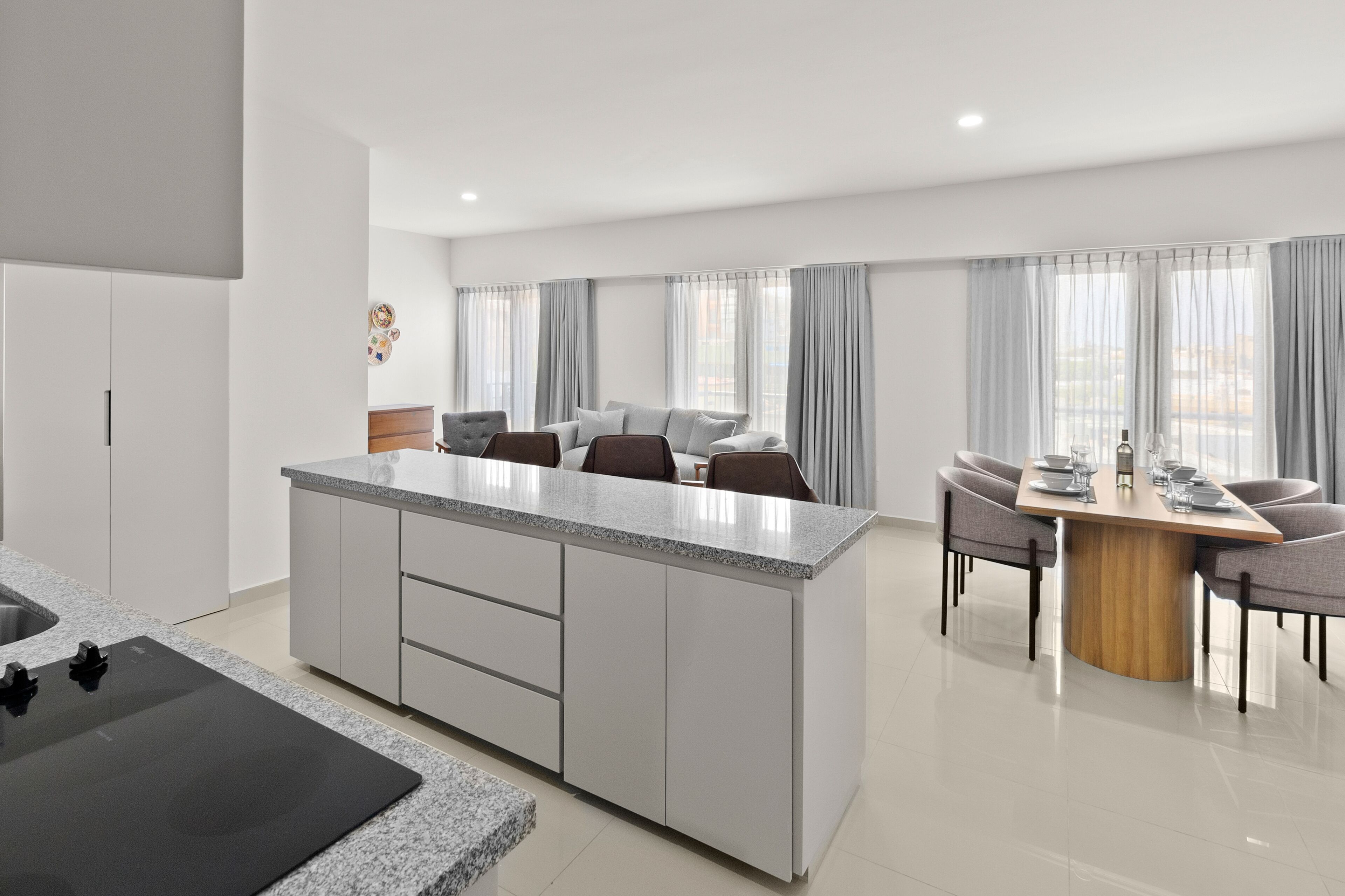 A modern kitchen with a central island, dining area with a table and chairs, and a view of the outside through large windows.