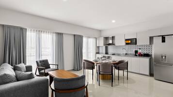 Una sala de estar moderna con sofá y sillones, un comedor con mesa y sillas, y una cocina con electrodomésticos y salpicadero de azulejos.