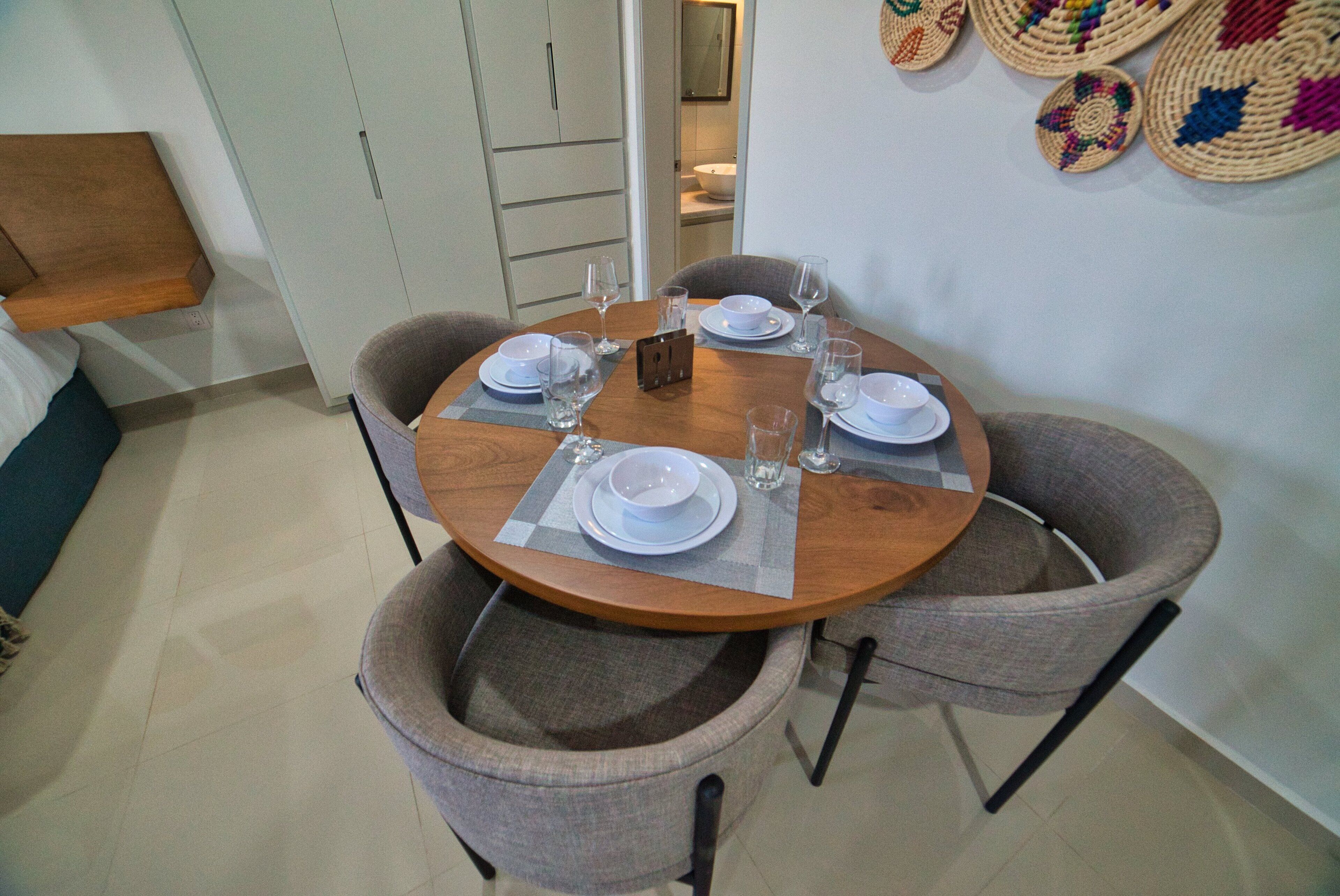 A dining area with a round table set for four, surrounded by four grey upholstered chairs.