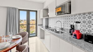 A modern kitchen with a large window, a dining area with a table set for two, and a city view. - Casa Barros Vacation Condos (Mazatlán)
