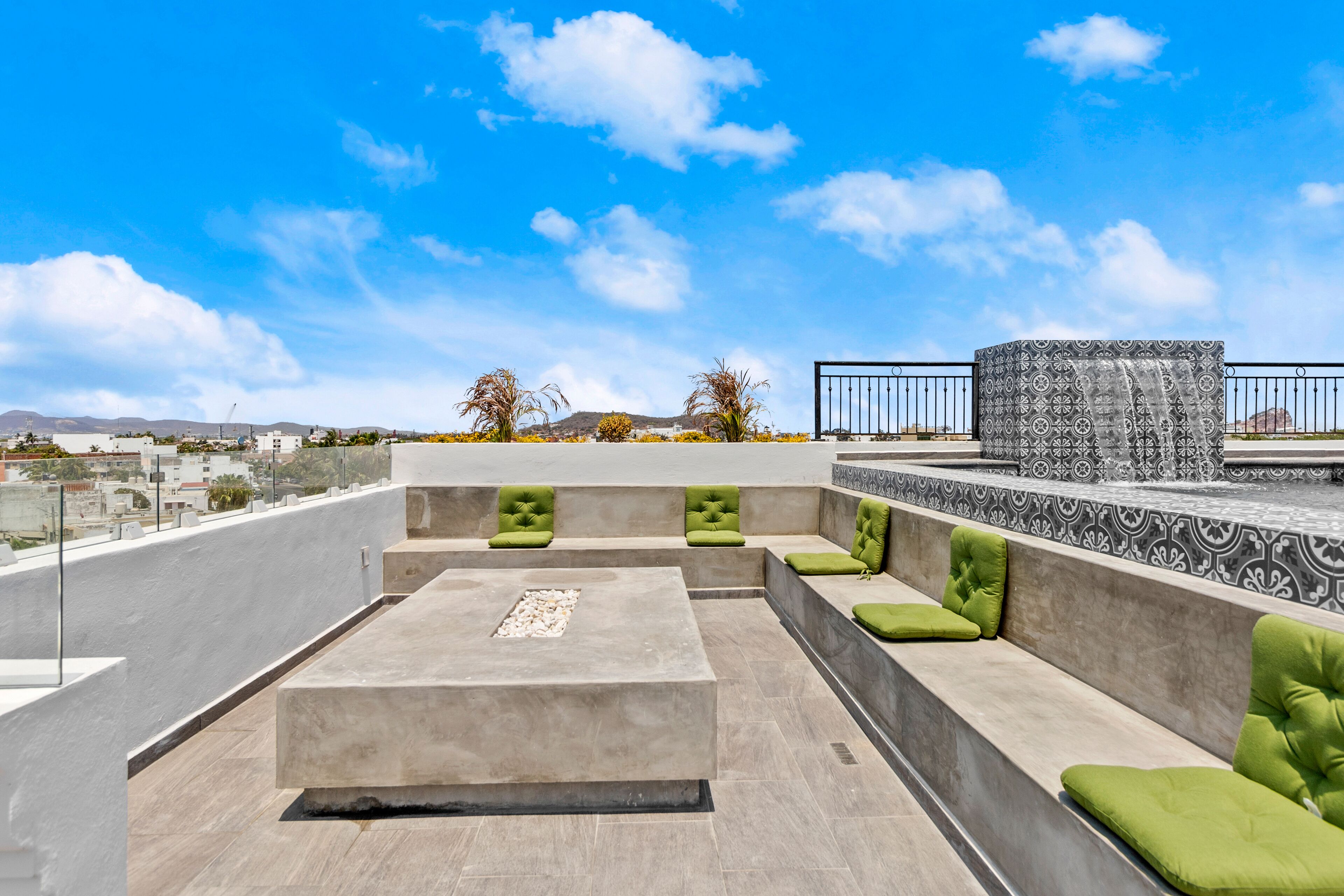 A rooftop terrace with seating areas, a patterned column, and a view of the cityscape.