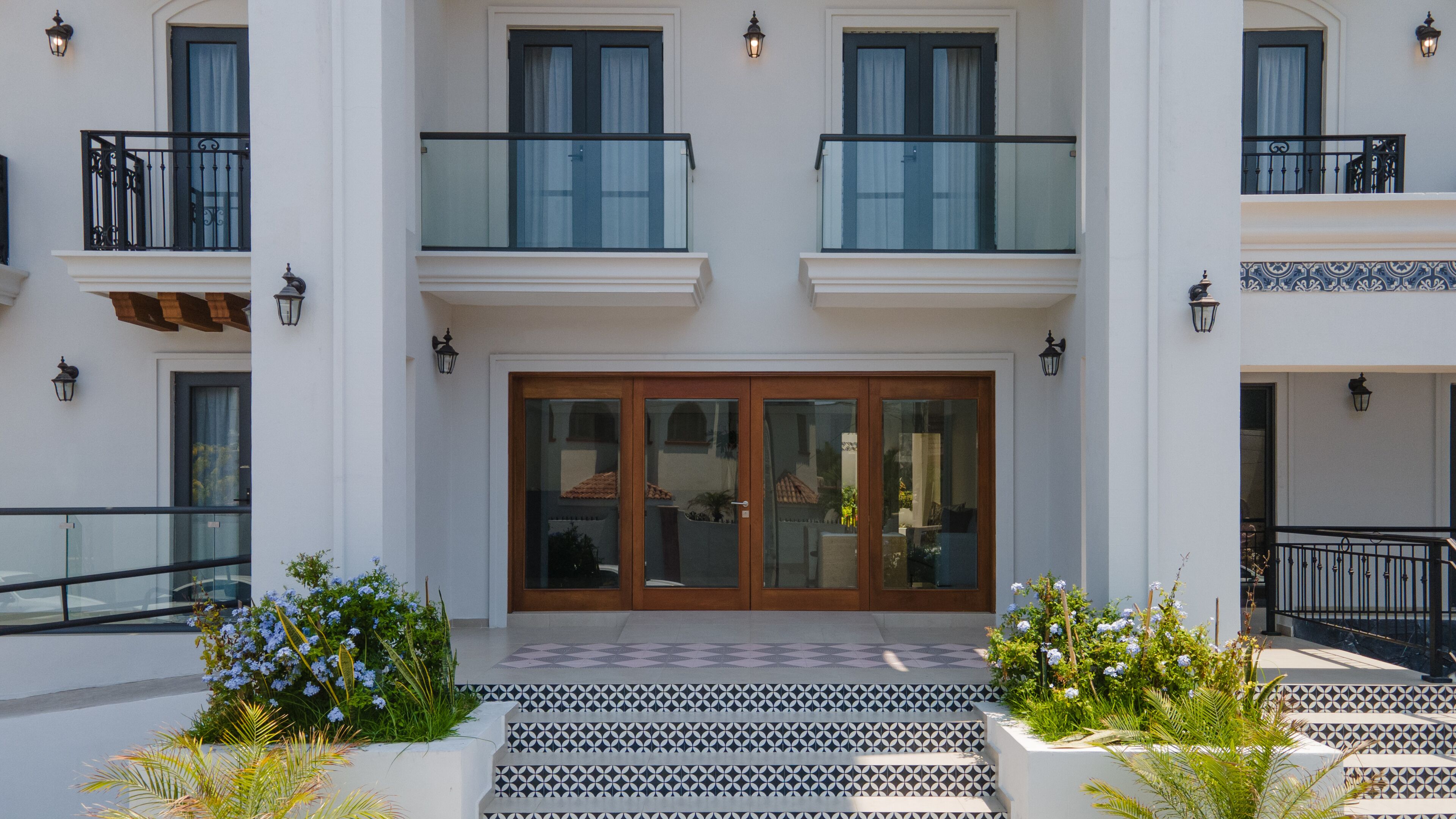 A two-story building with a central entrance, glass railings on the balconies, and a tiled entrance area.