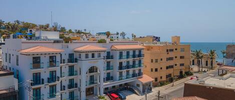 Un hotel de varios pisos con balcones, un estacionamiento y vista al mar.