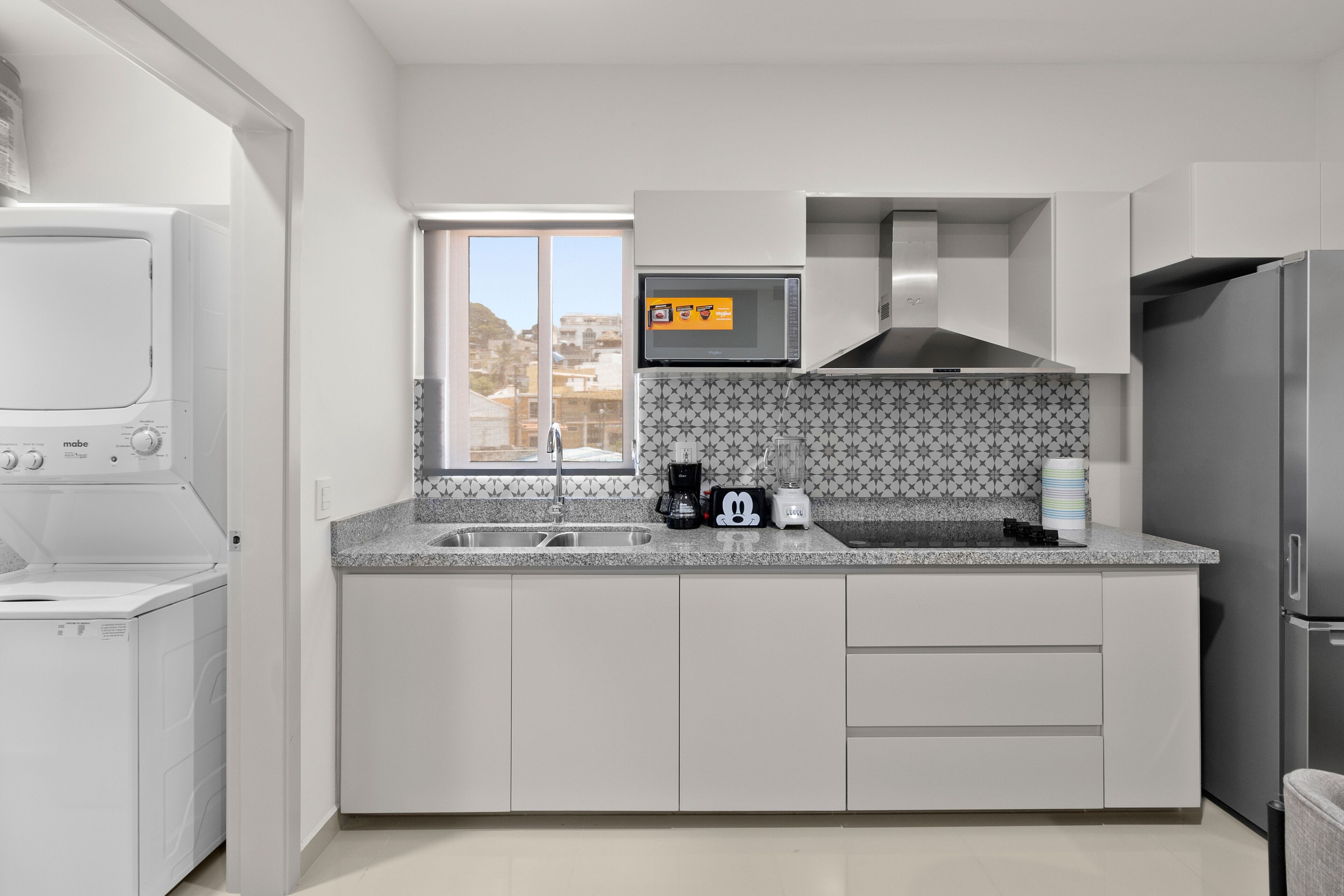 A modern kitchen with a built-in washer and dryer, a microwave, a coffee maker, and a refrigerator.