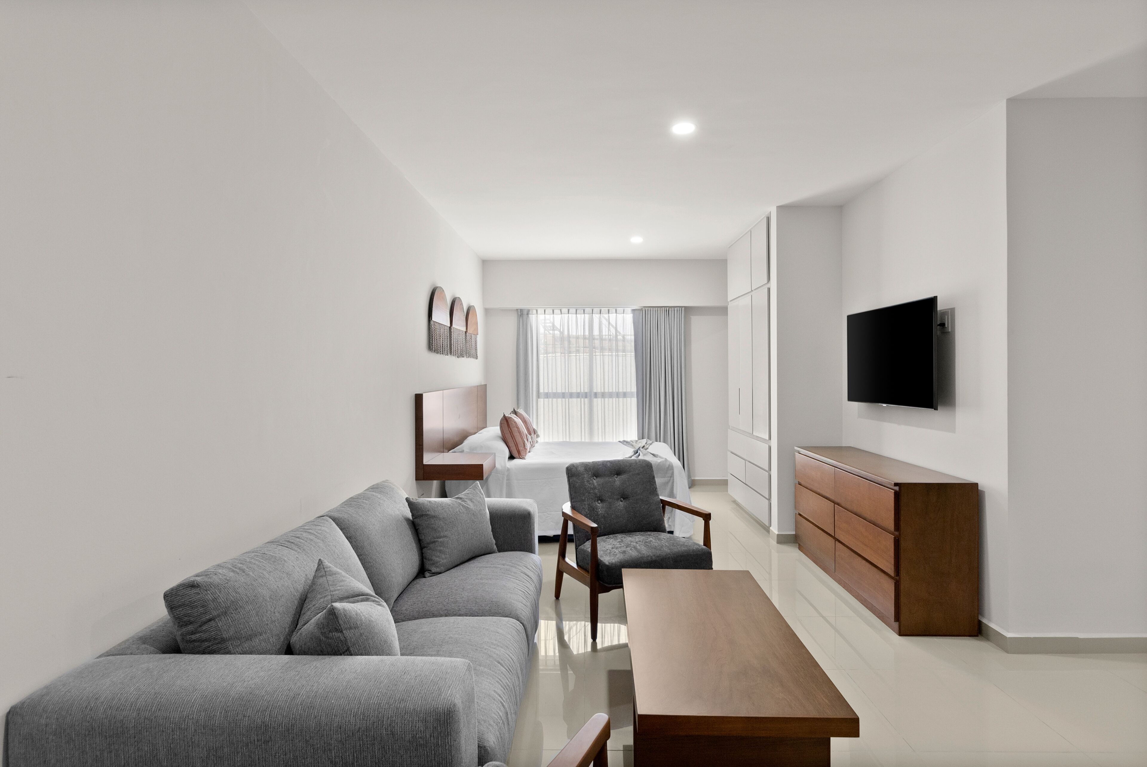 A modern living room with a sofa, armchair, coffee table, and a TV mounted on the wall.