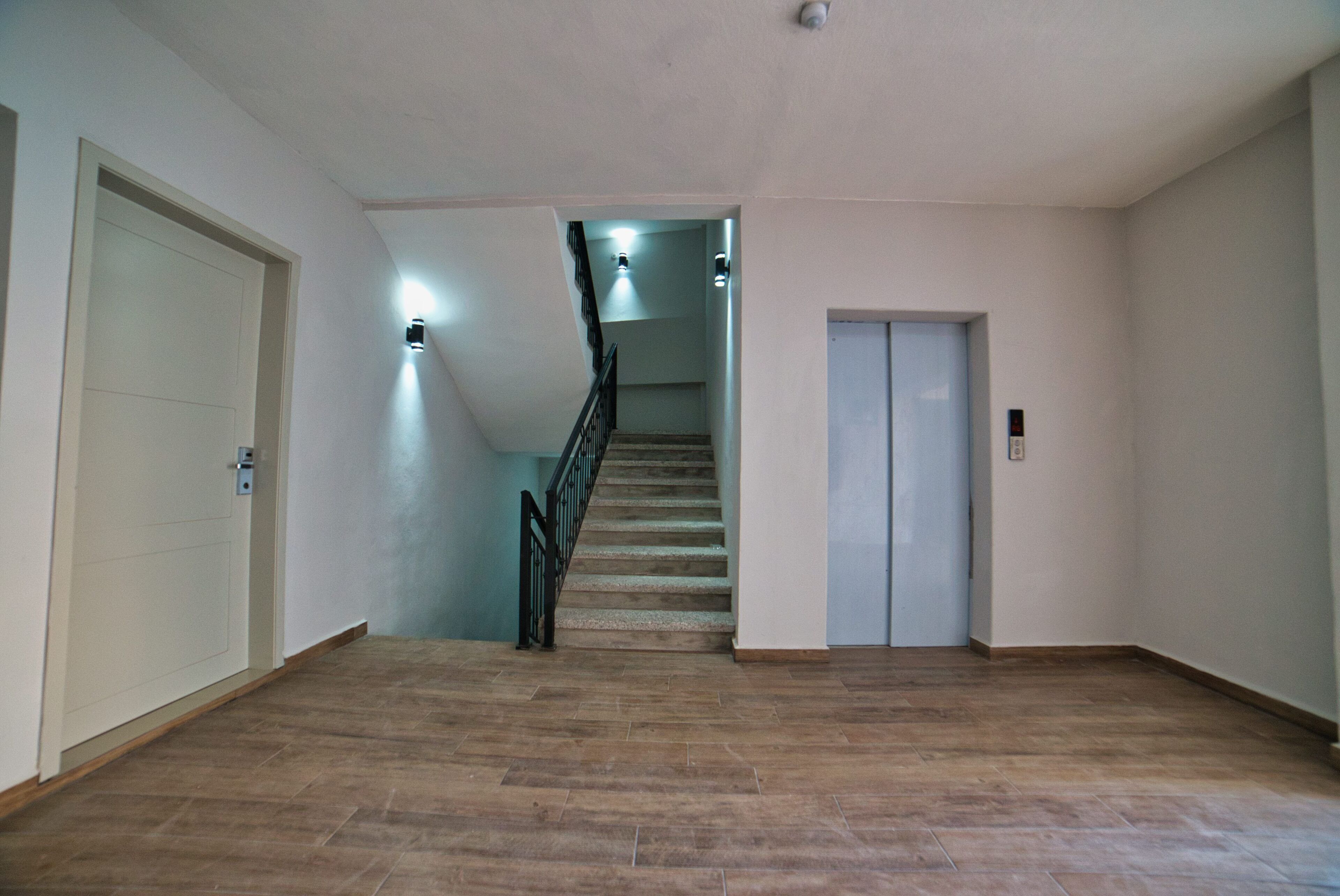 Un hall d’entrée spacieux avec un plancher en bois, un escalier doté d’une rampe noire et deux portes.