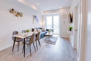 A modern living room with a dining area, a sofa, and a TV mounted on the wall. - Stylish Open Concept Condo w/Gym (Kitchener)