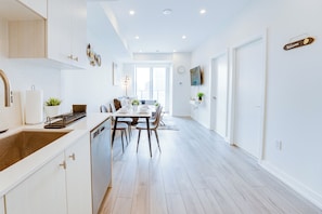 A modern kitchen with white cabinetry, a dining area with a table and chairs, and a living space with a TV and decorative items. - Stylish Open Concept Condo w/Gym (Kitchener)