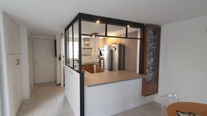 Una cocina moderna con refrigerador incorporado, un comedor con mesa y sillas, y un pasillo que lleva a una puerta.