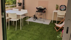 Un patio con una mesa y sillas blancas, una parrilla y un dardo.