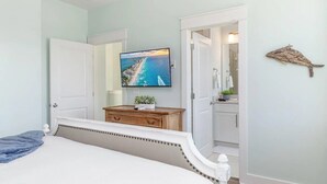 Ein Schlafzimmer mit einem Bett, einem an der Wand montierten Fernseher, einer Holzkommode und einer Tür zu einem Badezimmer.