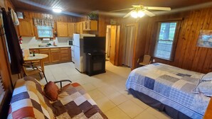 A compact cabin-style room with a kitchenette, a bed with a quilt, and a ceiling fan. - Lake View Cabin on Lake Norfork (Mountain Home)