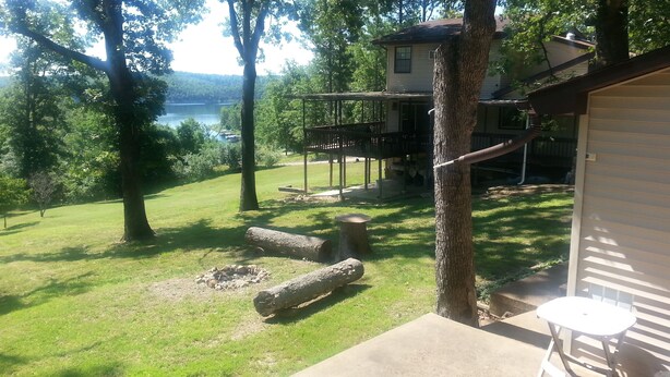 A backyard with a wooden deck, a stone fire pit, and a view of a lake. - Lake View Cabin on Lake Norfork (Mountain Home)