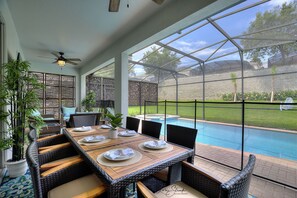 A covered patio with a pool, wicker furniture, and a table set for dining.