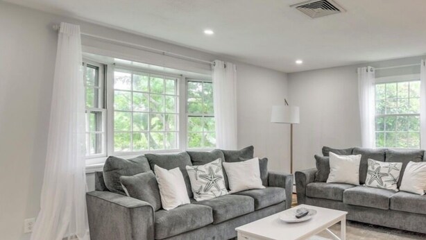 A modern living room with two grey sofas, a white coffee table, and large windows with white curtains. - Beautiful House near Beach and Castle Hill (Middletown)