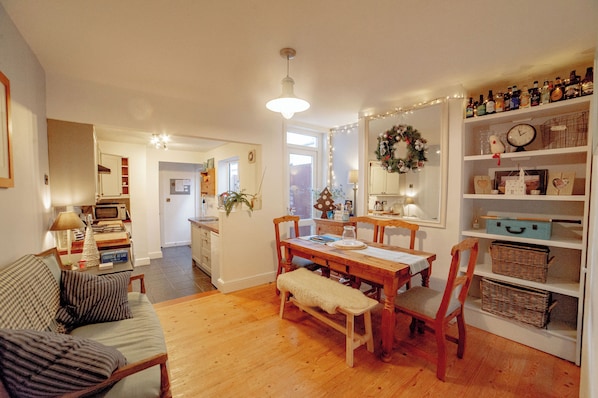 Una sala de estar acogedora con una mesa de comedor de madera, un banco y un sofá. Se observa un área de cocina al fondo, con un microondas y un refrigerador.