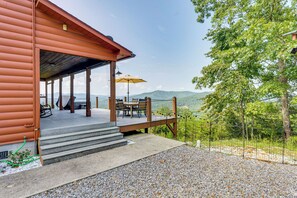 Una cabaña de madera con porche cubierto, mobiliario exterior y vistas a las montañas.