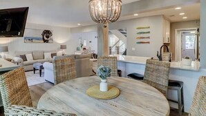 Un salon moderne avec une table à manger ronde, des chaises en osier, un lustre et un téléviseur à écran plat fixé au mur.