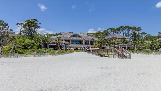 Une propriété située en bord de mer, comprenant un grand bâtiment, une plage de sable et un escalier en bois menant au bâtiment.