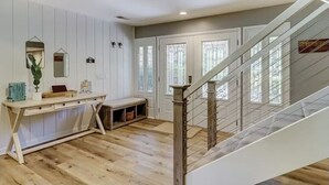 Un intérieur moderne avec un plancher en bois, une console blanche, un banc et un escalier doté d’une rampe en métal.