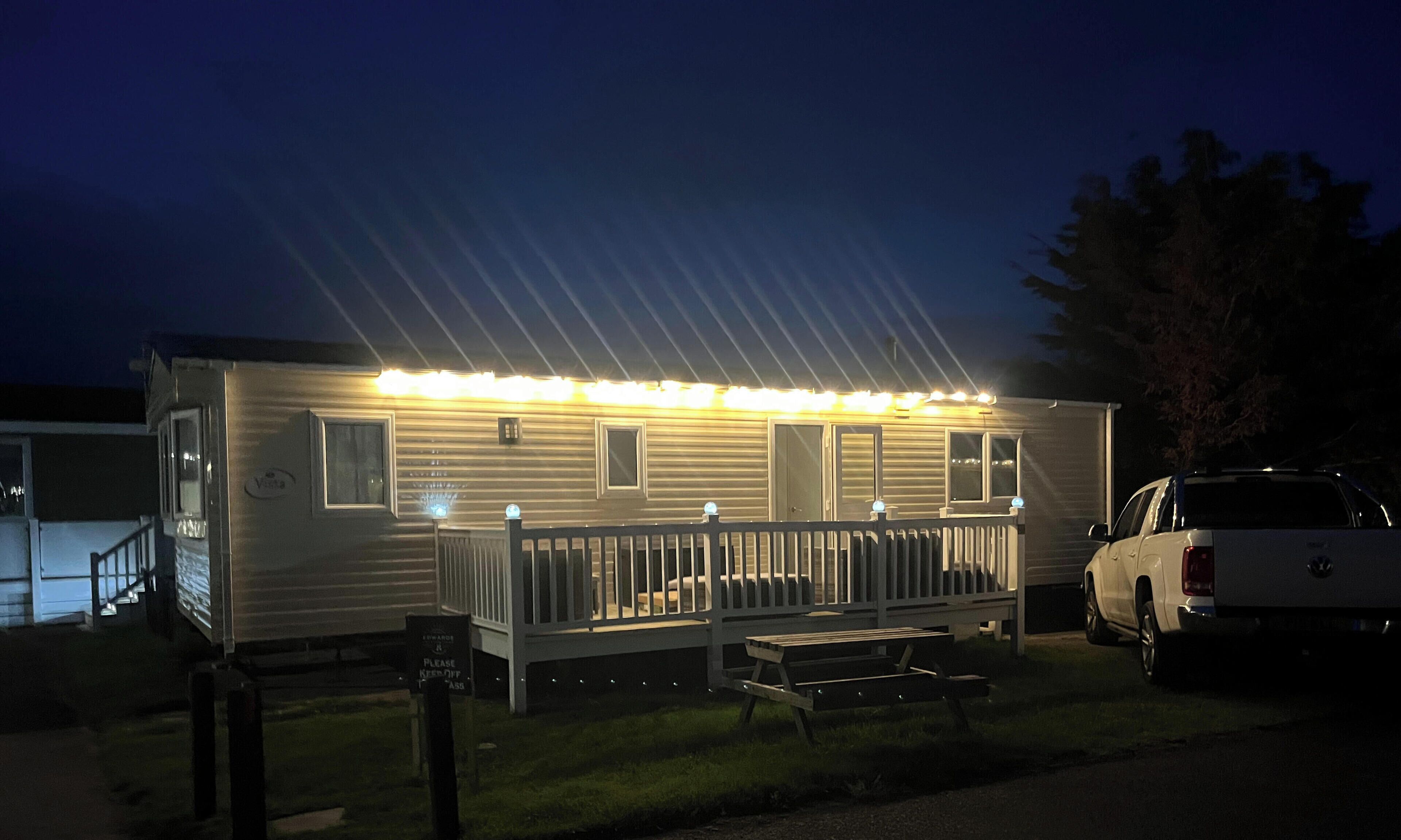 A mobile home with a porch, a bench, and a parked SUV.