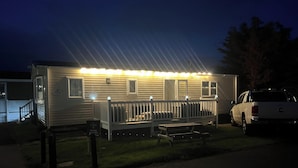 Une maison mobile avec une véranda, un banc et un VUS garé.