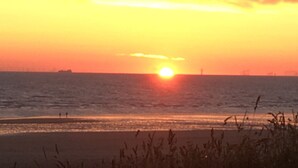 Un coucher de soleil sur l’océan, avec un navire au loin et un phare.