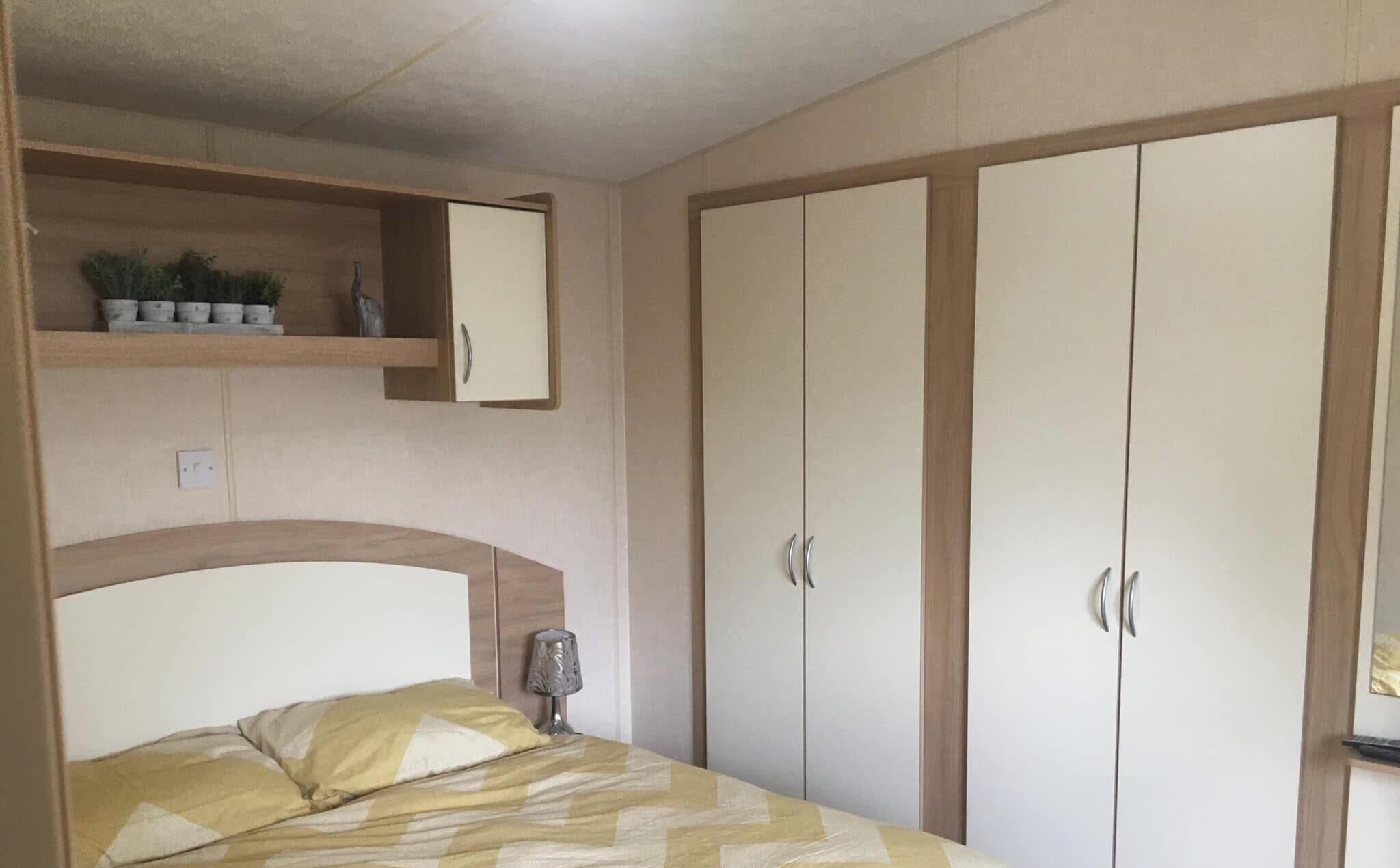 A bedroom with a bed, a bedside lamp, a shelf with plants, and a wardrobe with two doors.