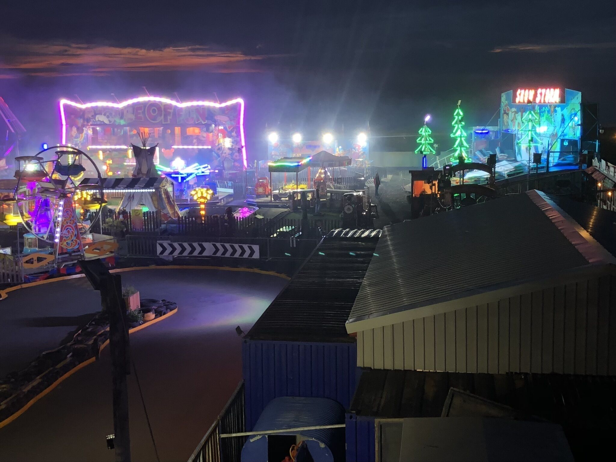 Un parc d’attractions nocturne proposant diverses attractions et manèges, notamment une grande roue et un espace sur le thème de la neige.
