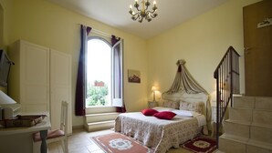 Un dormitorio con cama, escritorio, silla, ventana con cortinas, candelabro y escalera.