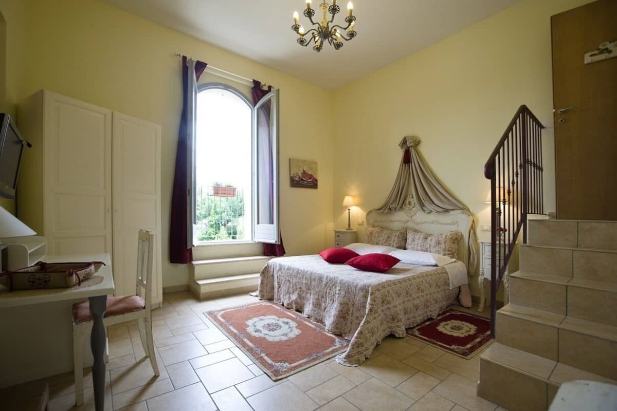 Une chambre à coucher comprenant un lit, un bureau, une chaise, une fenêtre avec des rideaux, un lustre et un escalier.
